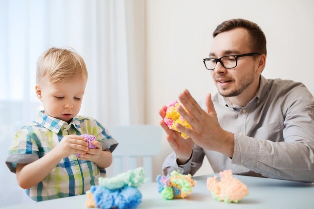 家族、子供時代、創造性、活動、人のコンセプト – 幸せな父と幼い息子が家でボール粘土で遊ぶ