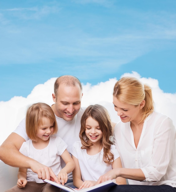 Photo family, childhood, dream and people - smiling mother, father and little girls reading book over blue sky and cloud background