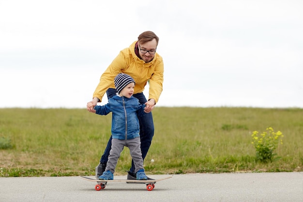 가족, 유년기, 부성애, 레저, 사람 개념 - 어린 아들에게 스케이트보드를 타도록 가르치는 행복한 아버지