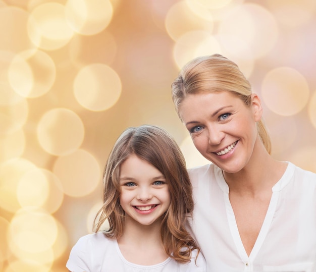 Foto famiglia, infanzia, felicità e persone - madre sorridente e bambina su sfondo di luci beige