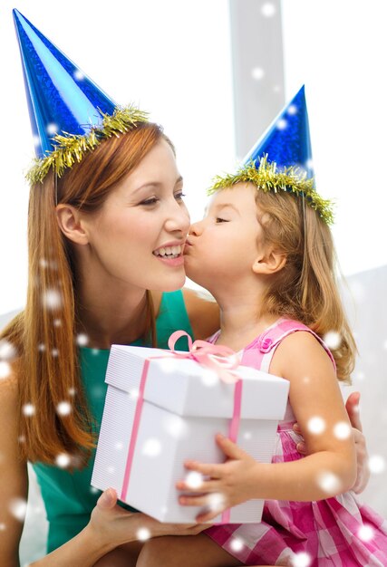 family, childhood, holidays and people concept - happy mother and daughter in blue party hats with gift box