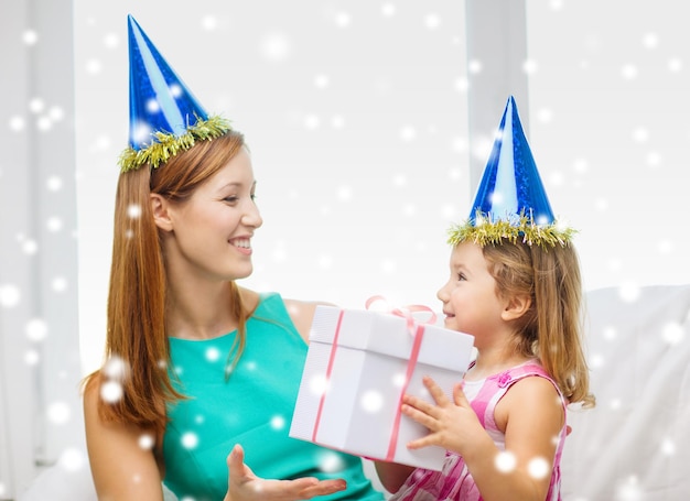 Concetto di famiglia, infanzia, vacanze e persone - madre e figlia felici in cappelli da festa blu con confezione regalo