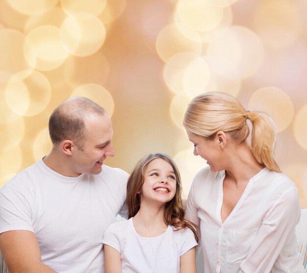 family, childhood, holidays and people - smiling mother, father and little girl over beige lights background