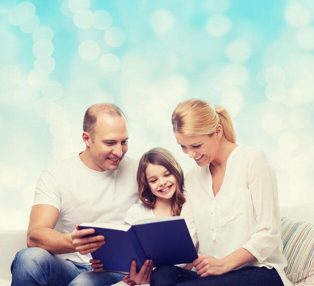 Photo family, childhood, holidays and people - smiling mother, father and little girl reading book over blue lights background