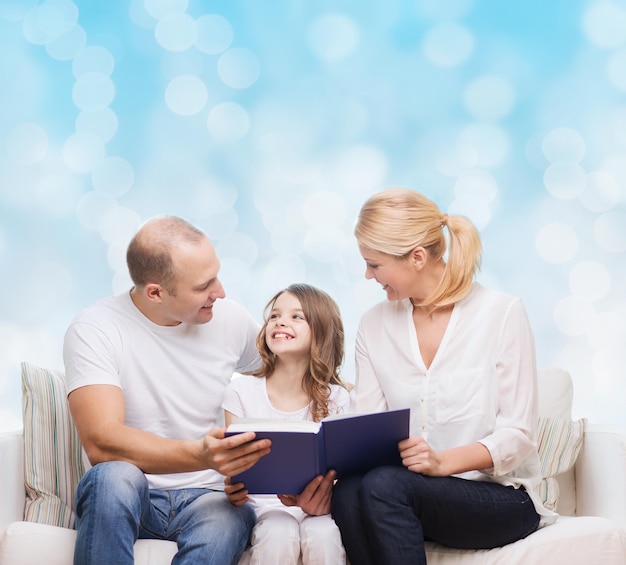 семья, детство, праздники и люди - улыбающиеся мать, отец и маленькая девочка читают книгу на фоне голубых огней