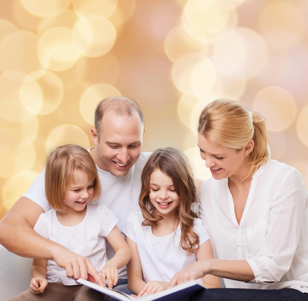 family, childhood, holidays and people - smiling mother, father and little girls reading book over beige lights background