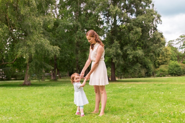 family, childhood and parenthood concept - happy mother with little baby girl playing and having fun at summer park