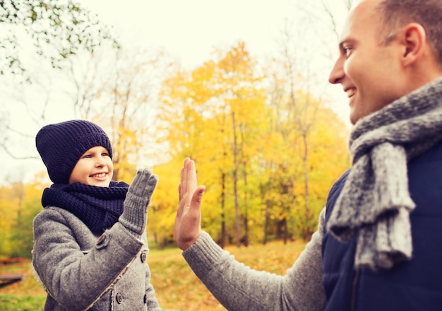 家族、子供時代、季節、ジェスチャー、人々の概念-秋の公園でハイタッチをする幸せな父と息子