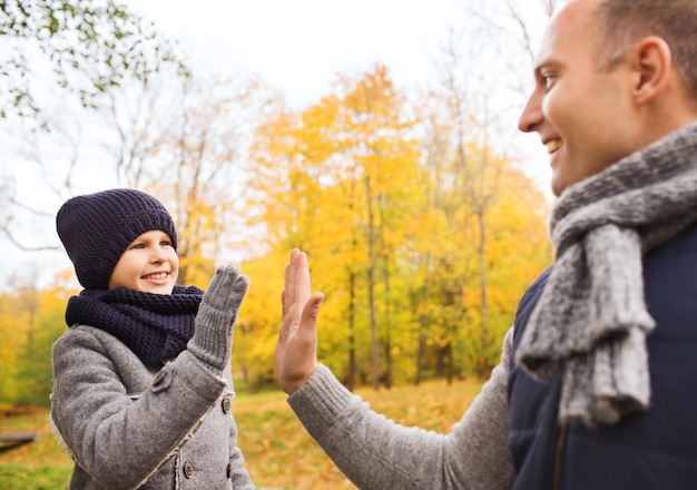 Concetto di famiglia, infanzia, stagione, gesto e persone - padre e figlio felici che fanno il cinque nel parco autunnale