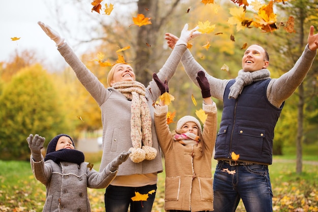 family, childhood, season and people concept - happy family playing with autumn leaves in park