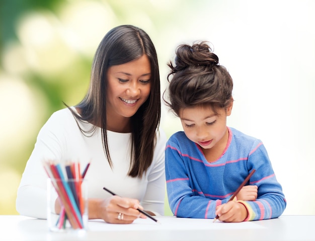 family, children, creativity and happy people concept - happy mother and daughter drawing with pencils over green background