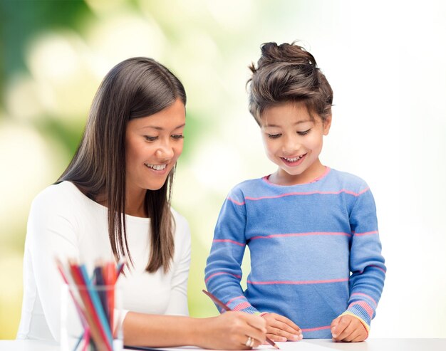 family, children, creativity and happy people concept - happy mother and daughter drawing with pencils over green background