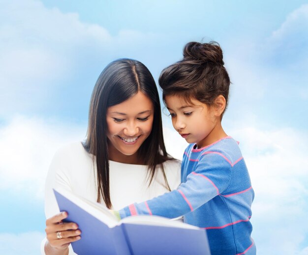 семья, дети, образование, школа и концепция счастливых людей - счастливая мать и дочь читают книгу на фоне голубого неба