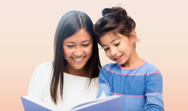 family, children, education, school and happy people concept - happy mother and daughter reading book over pink background