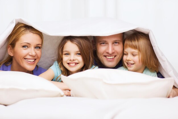 Foto concetto di famiglia, bambini e casa - famiglia felice con due bambini sotto la coperta a casa