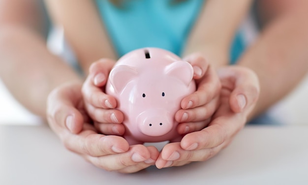 Family, children, money, investments and people concept - close\
up of father and daughter hands holding pink piggy bank