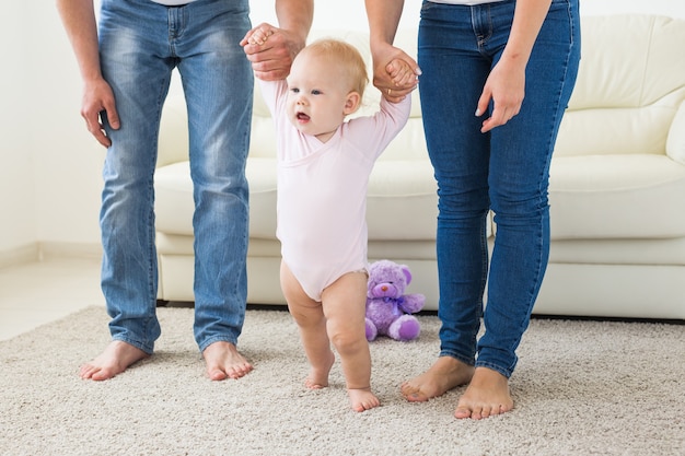 Photo family, children and parenthood concept - parents teaching baby girl to walk.