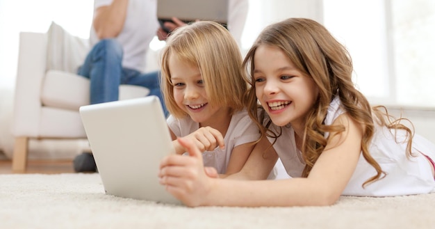 family, children, technology and home concept - smiling sister with tablet pc computer and parents on the back with laptop