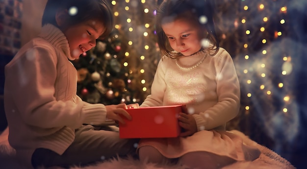 Famiglia alla vigilia di natale al caminetto. i bambini aprono i regali di natale. bambini sotto l'albero di natale con scatole regalo. soggiorno decorato con camino tradizionale. serata d'inverno calda e accogliente a casa.