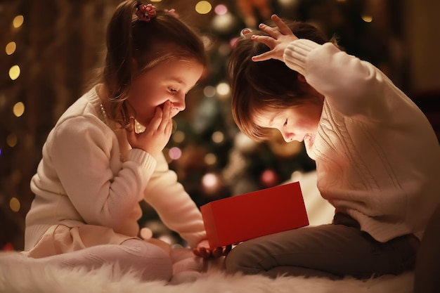 벽난로에서 크리스마스 이브에 가족입니다. 크리스마스 선물을 여는 아이들. 선물 상자가 있는 크리스마스 트리 아래 아이들. 전통적인 벽난로가 있는 장식된 거실. 집에서 아늑하고 따뜻한 겨울 저녁.