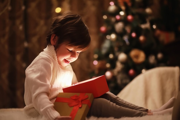 벽난로에서 크리스마스 이브에 가족 크리스마스를 여는 어린이 선물 상자가 있는 크리스마스 트리 아래 어린이 전통적인 벽난로가 있는 장식된 거실 집에서 아늑한 따뜻한 겨울 저녁