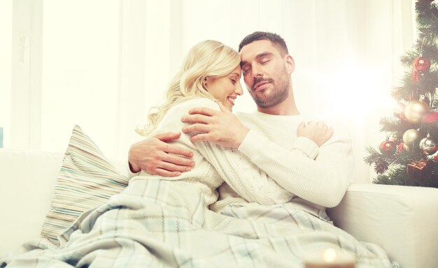 Photo family, christmas, holidays, love and people concept - happy couple covered with plaid sitting on sofa at home