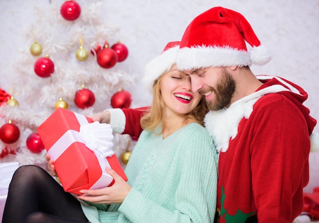 家族のクリスマスの伝統 一緒にクリスマスを祝う 愛情のあるカップルは、クリスマス ツリーの背景とプレゼントを開梱しながら笑みを浮かべて抱きしめる 愛のカップルは、クリスマスの休日のお祝いをお楽しみください