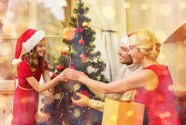 家族、クリスマス、x-mas、幸福と人々の概念-クリスマスツリーを飾るサンタヘルパー帽子で笑顔の家族