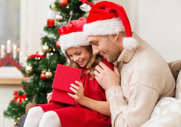 семья, рождество, рождество, счастье и концепция людей - улыбающиеся отец и дочь в шляпах помощников Санты открывают подарочную коробку