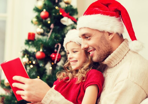 Family, christmas, x-mas, happiness and people concept - smiling father and daughter in santa helper hats reading book