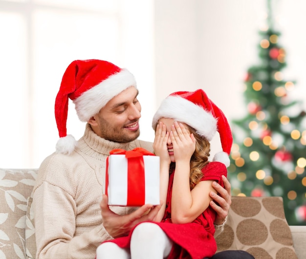 family, christmas, x-mas, winter, happiness and people concept - smiling daughter with closed eyes waiting for a present from fathe