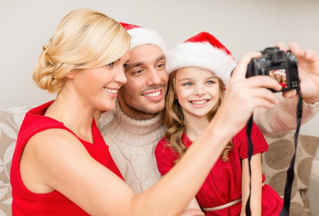 家族、クリスマス、クリスマス、冬、幸福と人々の概念-写真カメラで写真を撮るサンタヘルパー帽子で笑顔の家族