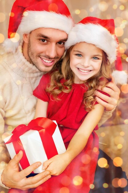 가족, 크리스마스, 크리스마스, 겨울, 행복, 사람 개념 - 선물 상자를 들고 산타 도우미 모자를 쓰고 웃고 있는 아버지와 딸