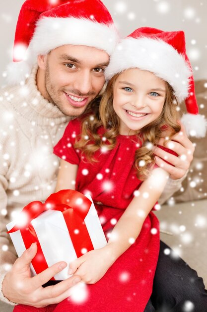 family, christmas, x-mas, winter, happiness and people concept - smiling father and daughter in santa helper hats holding gift box