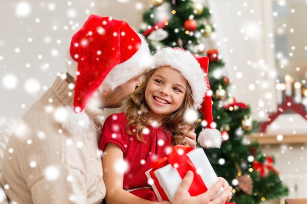 family, christmas, x-mas, winter, happiness and people concept - smiling father and daughter in santa helper hats holding gift box