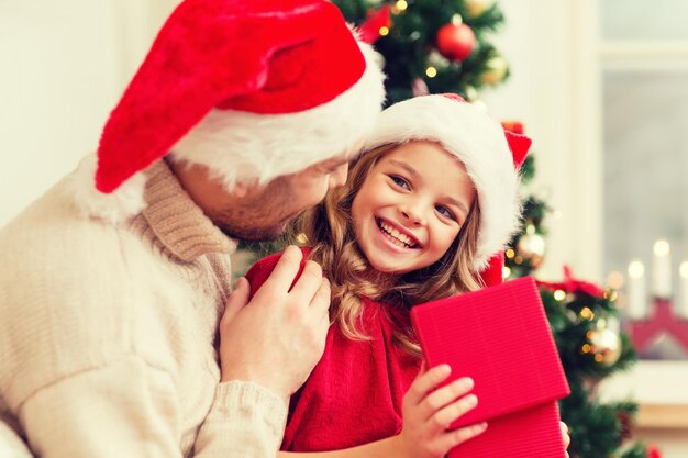 Family, christmas, x-mas, winter, happiness and people concept - smiling father and daughter in santa helper hats opening gift box