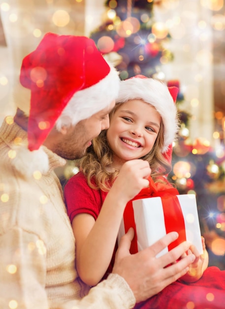 家族、クリスマス、クリスマス、冬、幸福と人々のコンセプト-サンタヘルパー帽子の笑顔の父と娘がギフトボックスを開く