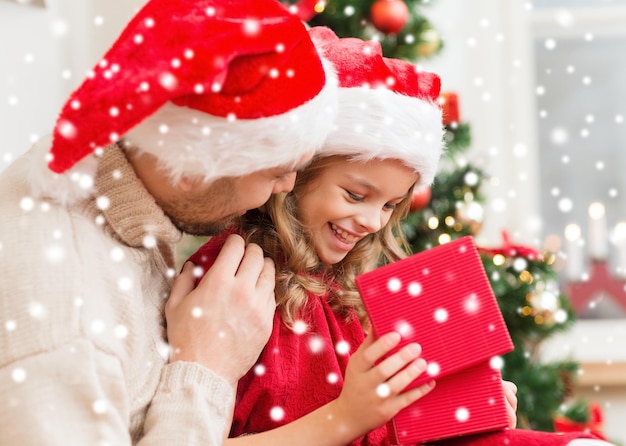 family, christmas, x-mas, winter, happiness and people concept - smiling father and daughter in santa helper hats opening gift box