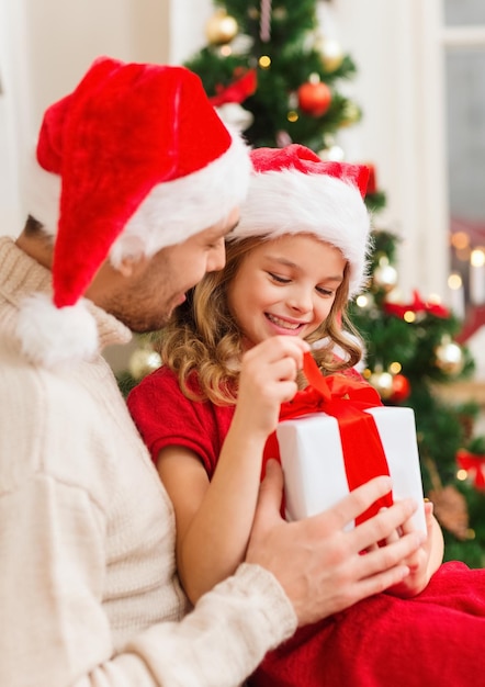 가족, 크리스마스, 크리스마스, 겨울, 행복, 그리고 사람들의 개념 - 선물 상자를 여는 산타 도우미 모자를 쓰고 웃고 있는 아버지와 딸