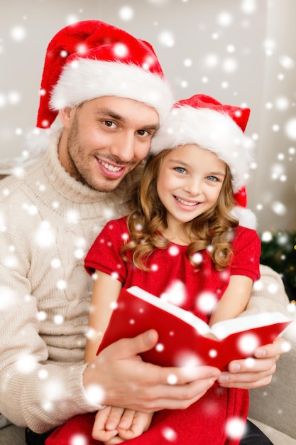 family, christmas, x-mas, winter, happiness and people concept - smiling father and daughter in santa helper hats reading book