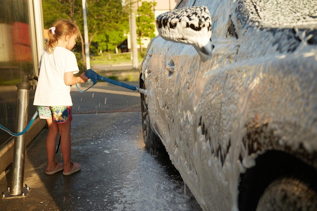 Family cleaning car in selfservice at car wash during sunset Car covered in white foam Concept of easy and fun selfservice