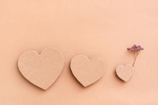 Family concept. Three cardboard hearts - parents and a child with a flower on a beige background. Top view. Copy space