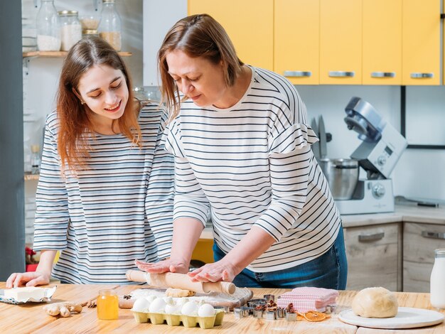 Family cooking hobby. Daughter watching her mom rolling dough, making gingerbread biscuits.