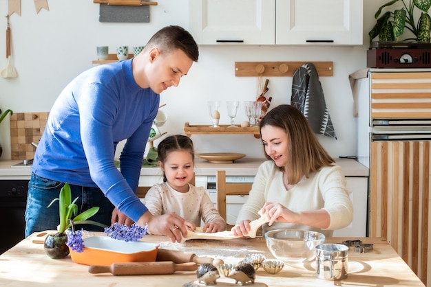 Cuochi di famiglia a casa mamma papà e figlia impastano insieme la pasta in una cucina uomo ragazza donna