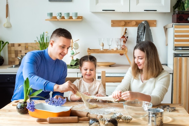 Family cooks at home mom dad and daughter knead the dough in a kitchen man girl woman together