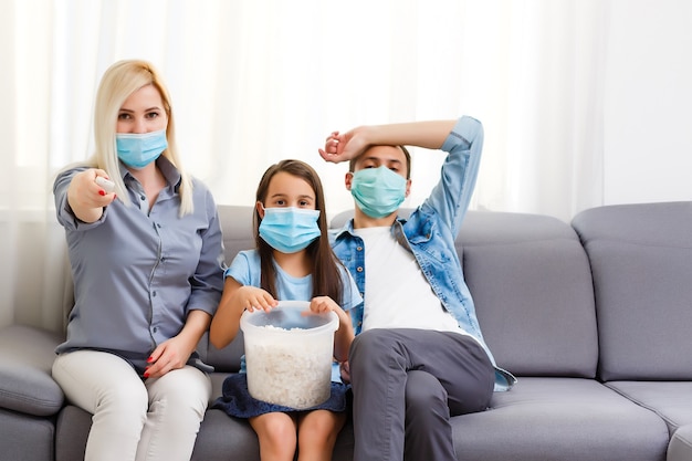 Family couple in medical face masks lying on a bed with a laptop. Concept of watching video, working together and quarantine during a COVID-19 coronavirus epidemic