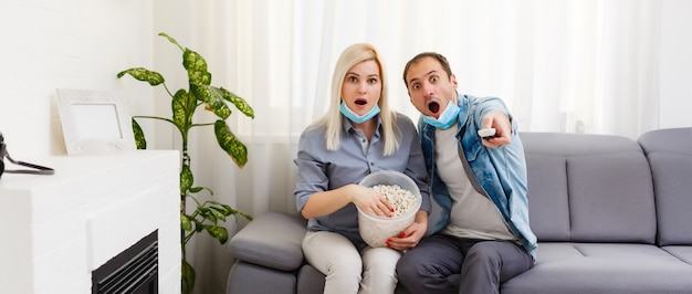 Family couple in medical face masks lying on a bed with a laptop. Concept of watching video, working together and quarantine during a COVID-19 coronavirus epidemic