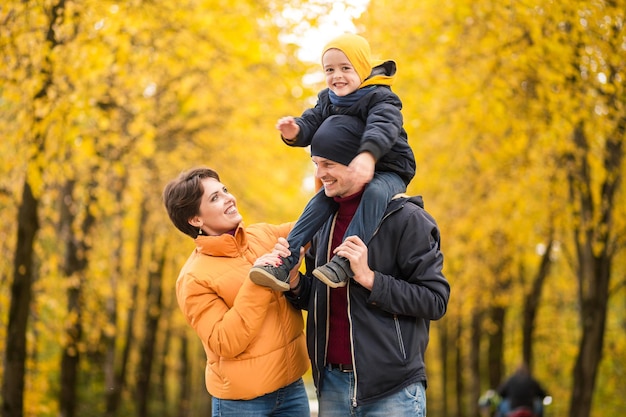 Coppia di famiglia in posa all'aperto con il loro bambino seduto sulle spalle dei padri