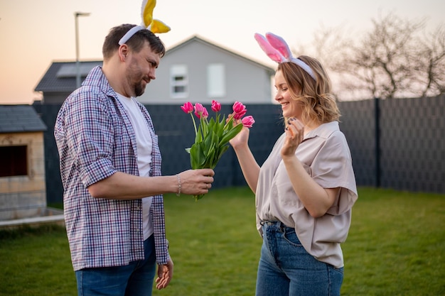 Coppia di famiglia che indossa orecchie da coniglio per celebrare la pasqua il marito regala a sua moglie tulipani