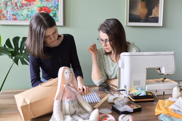 L'hobby e il tempo libero fatti a mano creativi della famiglia, la figlia dell'adolescente e della madre insieme cuciono la bambola del giocattolo del coniglietto. la donna insegna alla ragazza le abilità di cucito, parlando